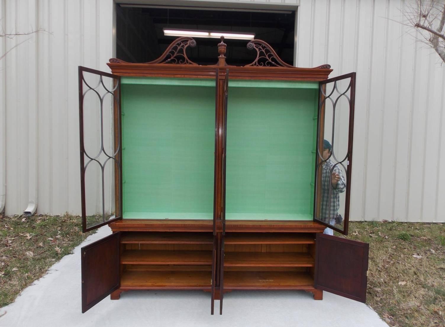 
English Regency yew and satinwood breakfront with carved floral medallions, broken arched fretwork pediment, carved centered urn, adjustable upper and lower interior shelving, original glass doors with arched mullions, and resting on inlaid oval