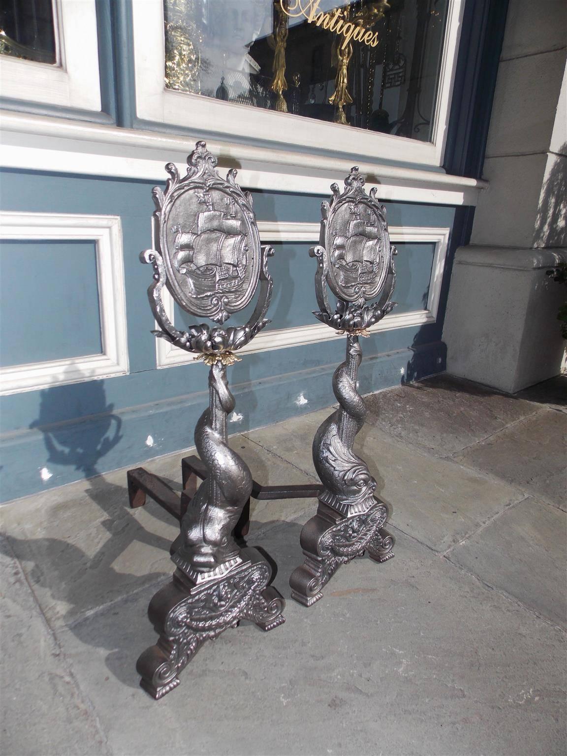 Pair of American polished steel and brass andirons with flanking oval ship medallion finials resting on a floral motif, flanking intertwined dolphins, and terminating on decorative swag bell flower plinths with scrolled feet, Mid-19th Century.
