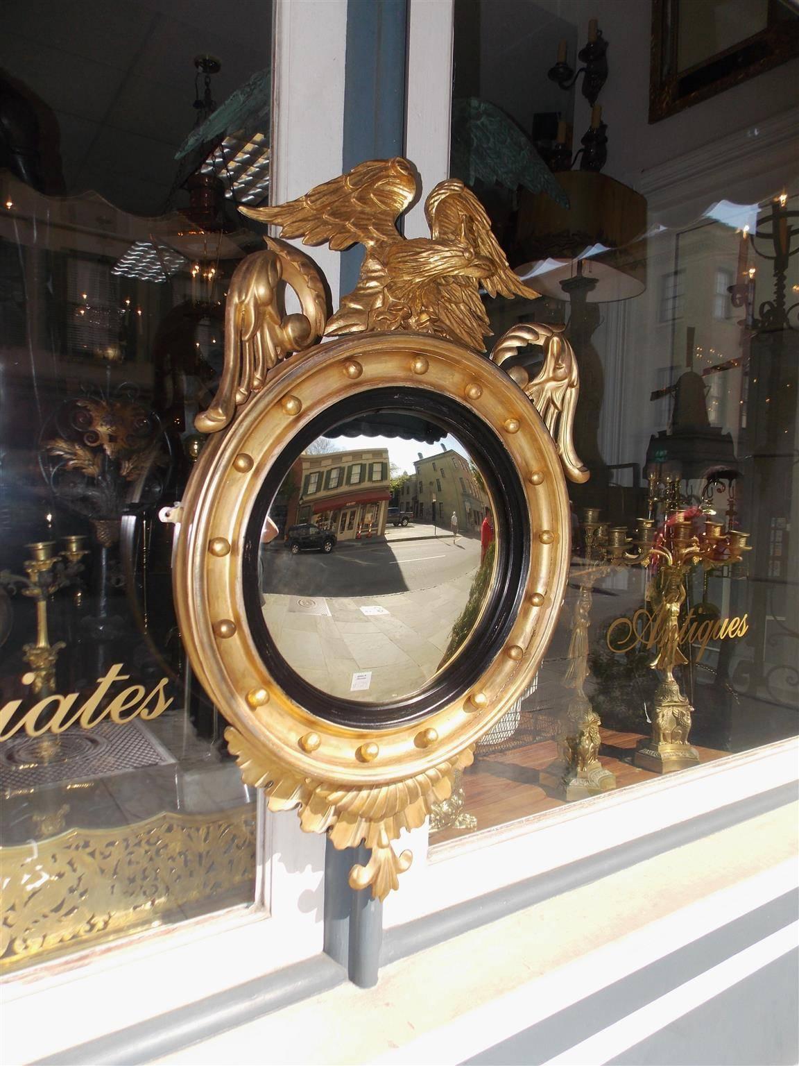 American gilt carved wood convex mirror with a perched eagle over flanking acanthus foliage, interior circular spheres, ebonized reeded ring, and terminating at bottom with acanthus floral pendant. Mirror retains the original glass and wood back,