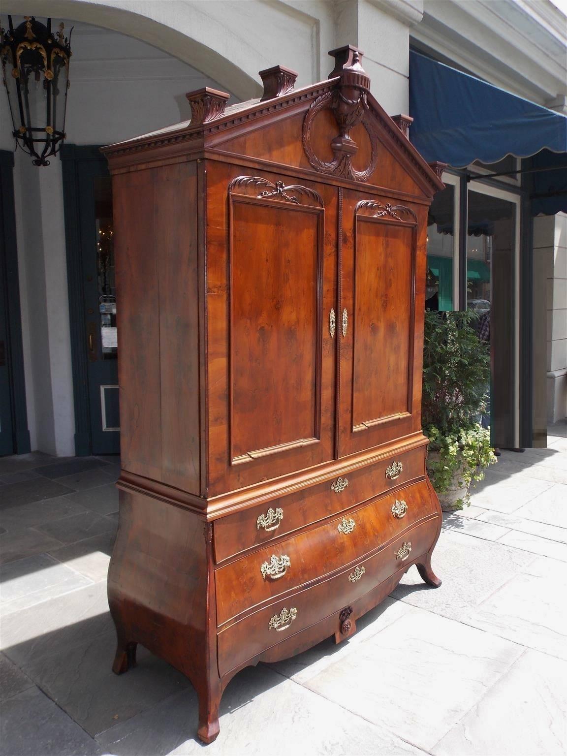 Dutch Yew Wood linen press with an upper case paladian acanthus cornice, centered urn with laurel wreath, dental molding, over flanking floral carved doors concealing a fitted interior shelving and three drawers. Press has a lower Bombay three