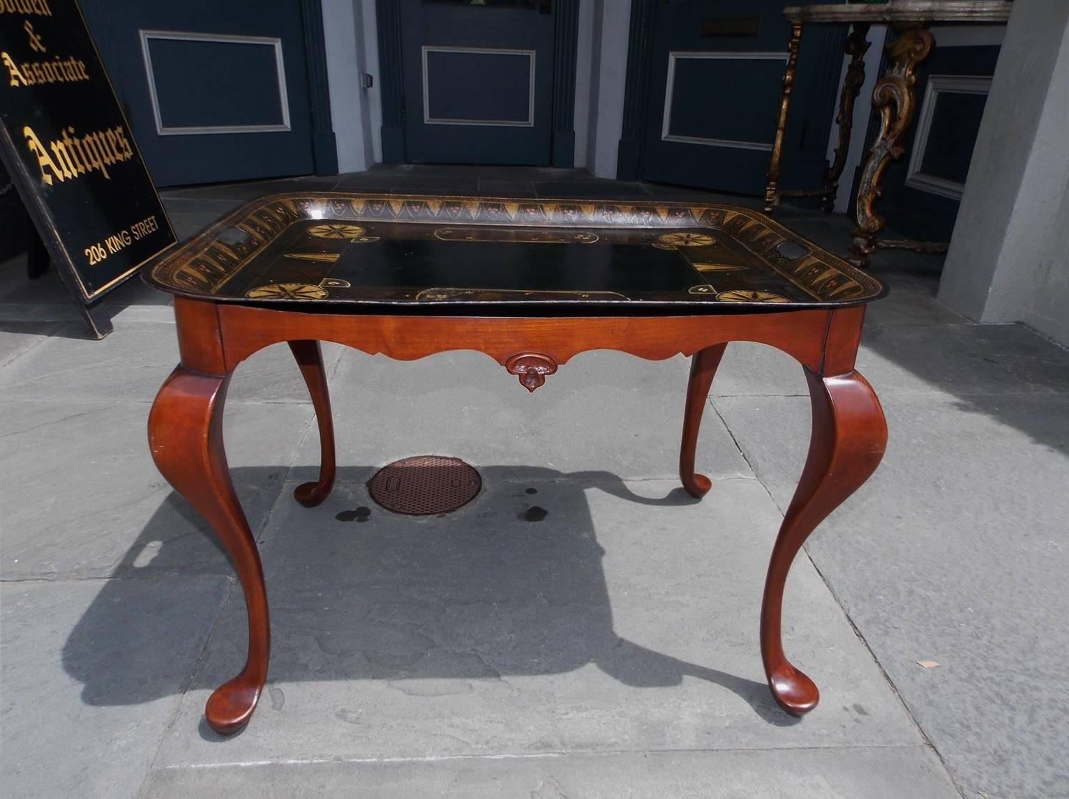 American hand-painted decorative tole tray on carved mahogany stand. Tray has two side handles with hand-painted floral, fruit and medallion motif. Stand was made for tray with a carved scalloped skirt, carved knee and terminating on stylized pad
