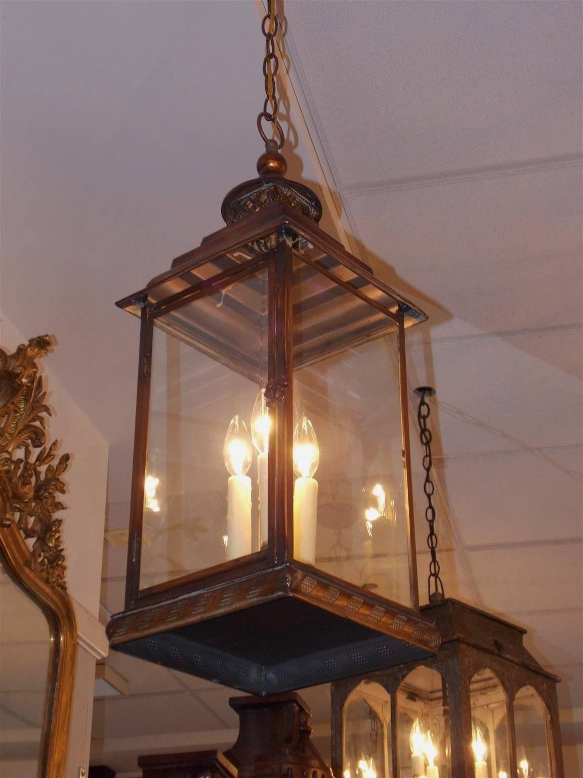English faux painted tin hanging lantern with a centered ring over beading, decorative floral swags, three-tiered step back, four glass sides with a hinged door, three-light cluster and terminating on a molded squared decorative beaded base, 20th
