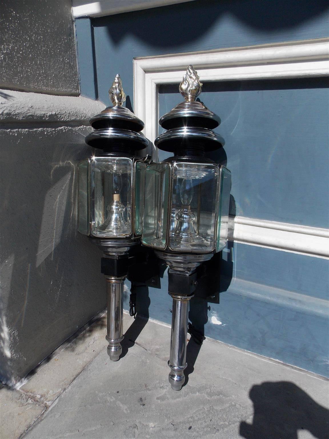 Pair of American nickel silver over brass coach lanterns with flame finials, tiered ringed tops, and terminate on a turned bulbous reservoir. Coach lanterns have the original eight sided beveled glass panels. White MFG. Company Bridgeport,