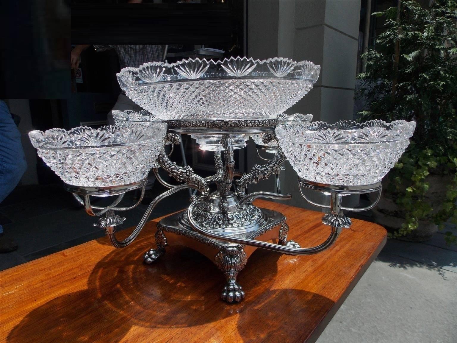 English Sheffield epergne with a centered cut crystal bowl, four scrolled arms with fitted crystal bowls, chased vine & berry motif throughout, and terminating on a squared base with acanthus & lions paw feet. Early 19th century.
