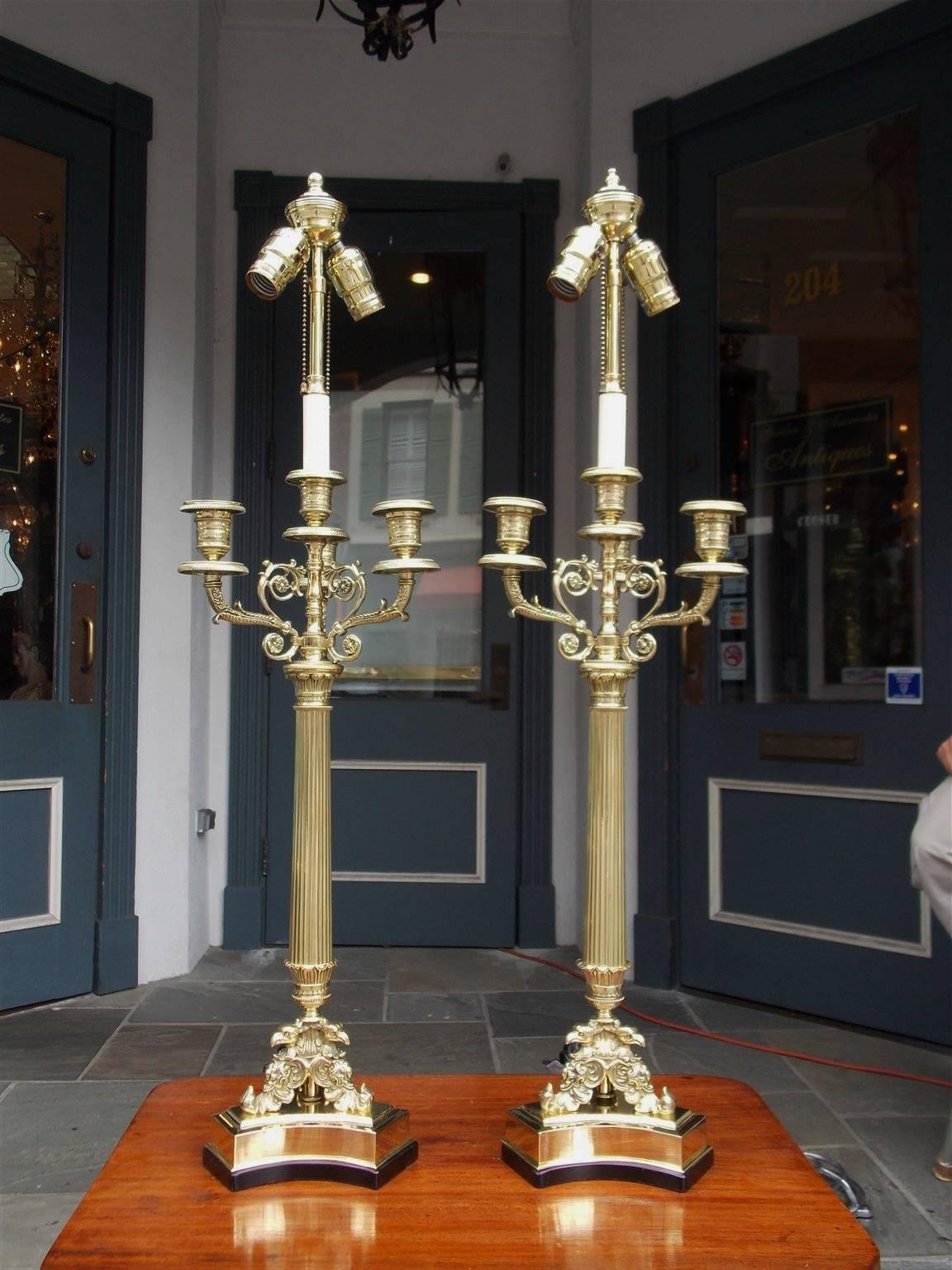 Pair of French brass candelabra lamps with four upper bobeches, decorative scrolled floral work and beaded hand chasing. Lamps have fluted centered columns and terminate on Eagle acanthus tripod painted wood bases, Early 19th century. Candelabras