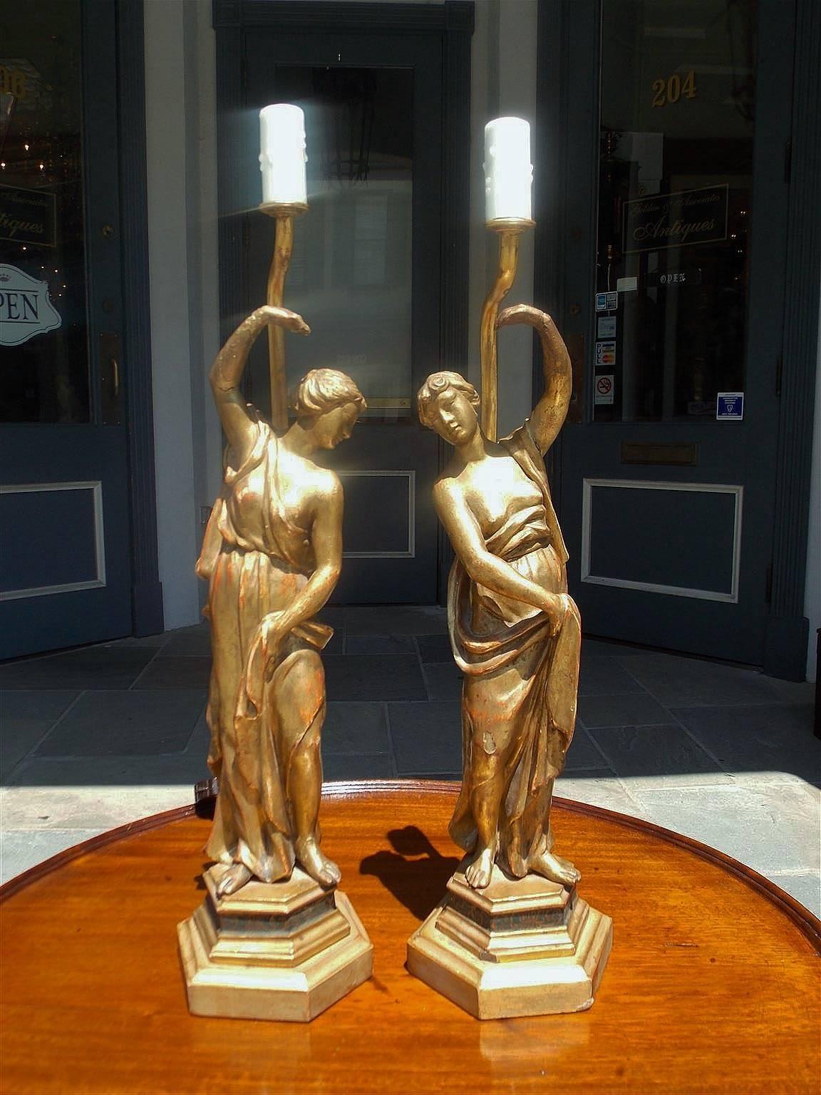 Pair of English gilt carved wood figural statues resting on floral poly chromed hexagon bases. Pair has been converted to single light lamps, Late 18th century.