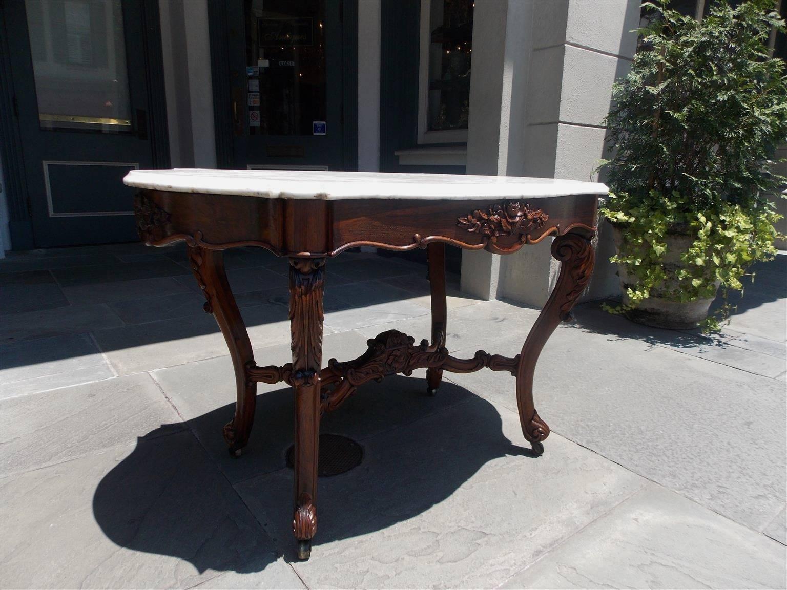 American rococo rosewood turtle top center table with carved floral skirt, original marble top, floral carved stretchers and terminating on acanthus carved scrolled legs with the original brass casters, Mid-19th century.