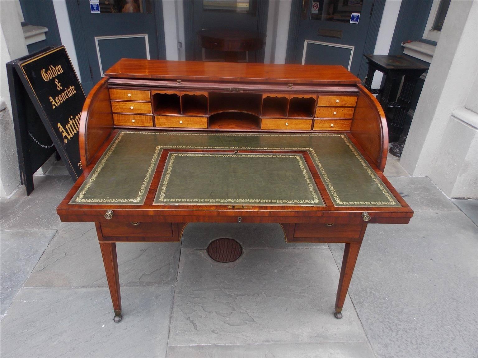 English mahogany tambour desk with sliding leather writing surface, interior satinwood compartmentalized drawers with the original bone knobs, five lower drawers with the original brasses over arched knee hole, ebonized string inlay and terminating