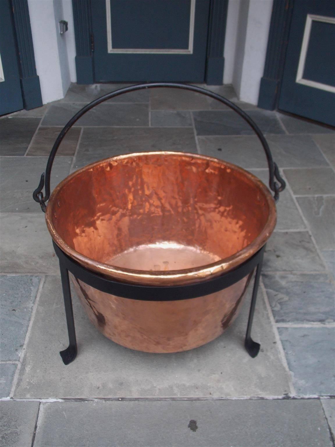 American monumental copper and wrought iron apple butter pot with original iron folding handle supported by circular fitted three leg stand with stylized splayed feet, Late 18th Century. Pot is 32