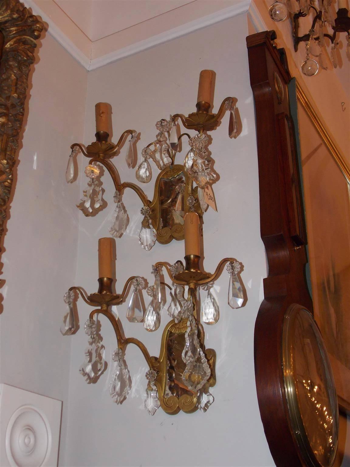 Zwei zweiarmige französische Wandleuchter aus vergoldeter Bronze und Kristall mit dekorativem Rankenwerk und verspiegelten Rückseiten. Die ursprünglich mit Kerzen betriebenen Wandleuchten wurden Ende des 19. Jahrhunderts elektrifiziert.