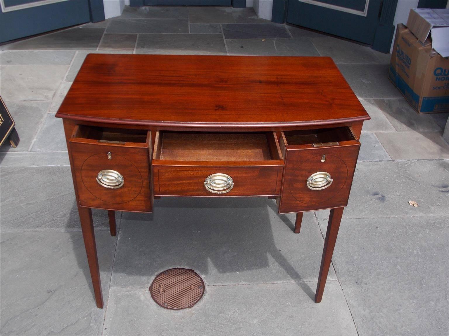 English mahogany bow front three-drawer lowboy / dressing table with arched centered knee hole, circular ebony string inlay, period brasses, and terminating on the original tapered squared legs, Early 19th Century.
