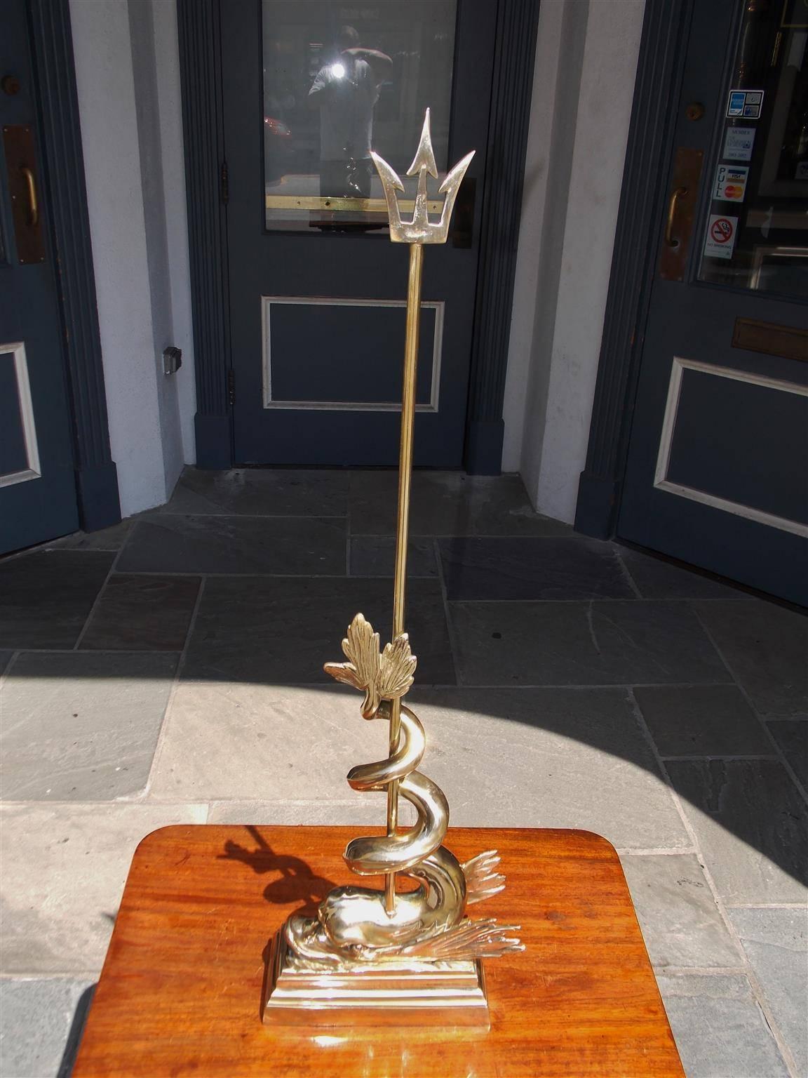 English brass winged dolphin intertwined trident doorstop resting on molded edge rectangular base, Early 19th Century.