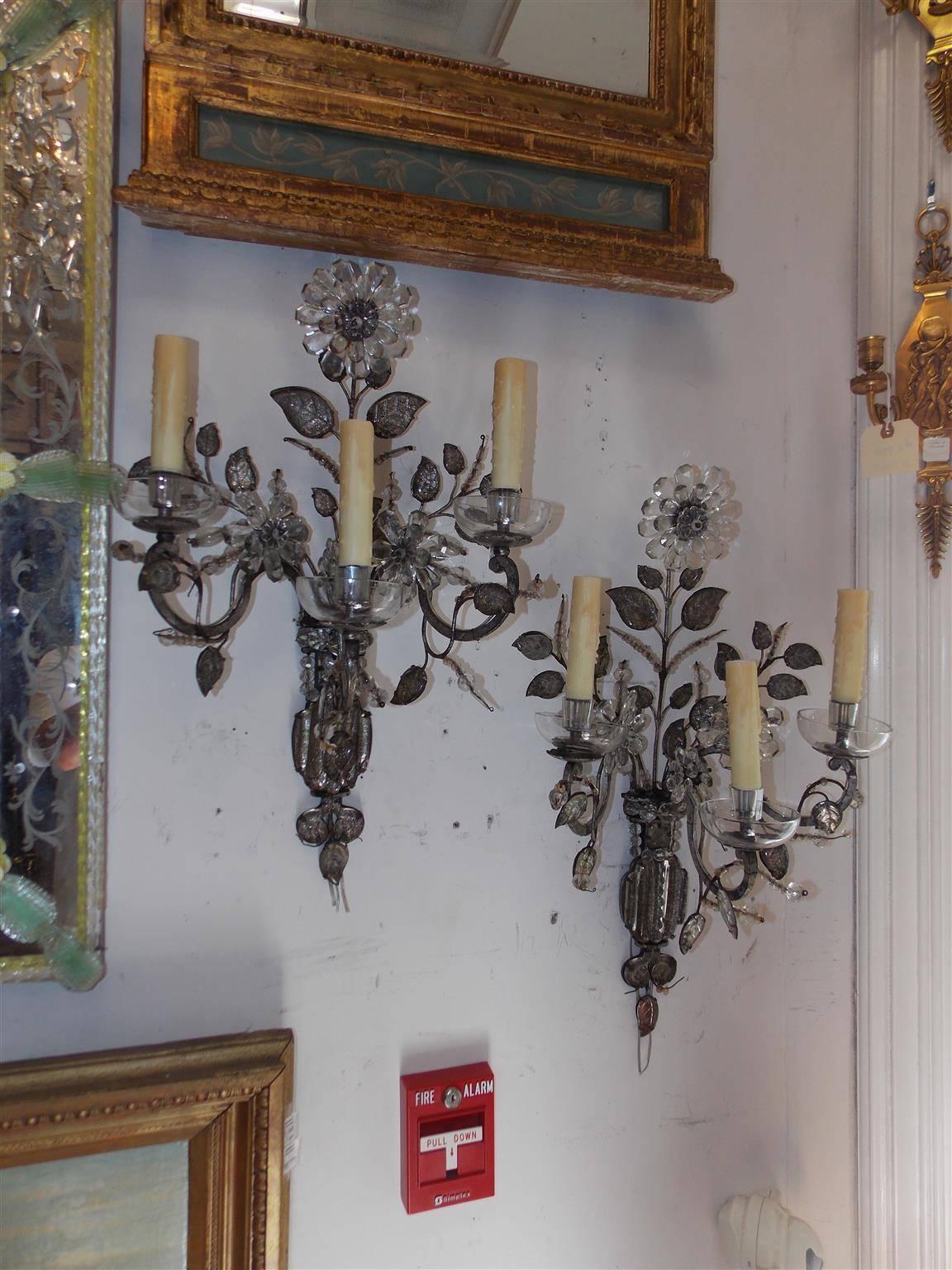 Pair of French Maison Baguès style three-arm crystal sconces with upper and centered floral medallions, bead work, leaf foliage and crystal cup bobeches. Sconces were originally candle powered and have been electrified, Late 19th Century.

Since