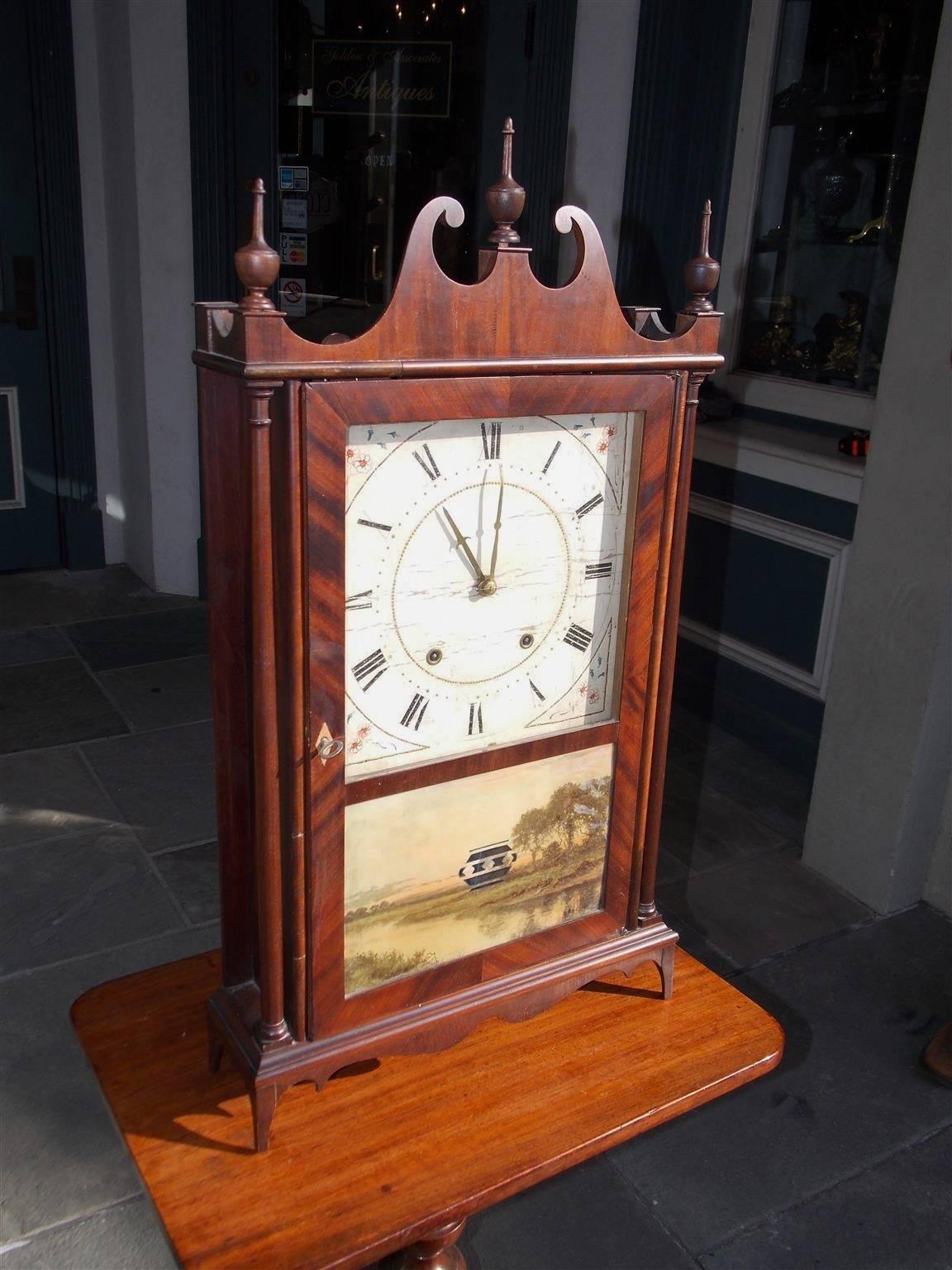 American Federal mahogany pillar and scroll mantel clock with a broken arch pediment, three urn wood finials, flanking ringed columns, hinged glass door with the original églomisé landscape painting, decorative hand-painted roman numeral face,