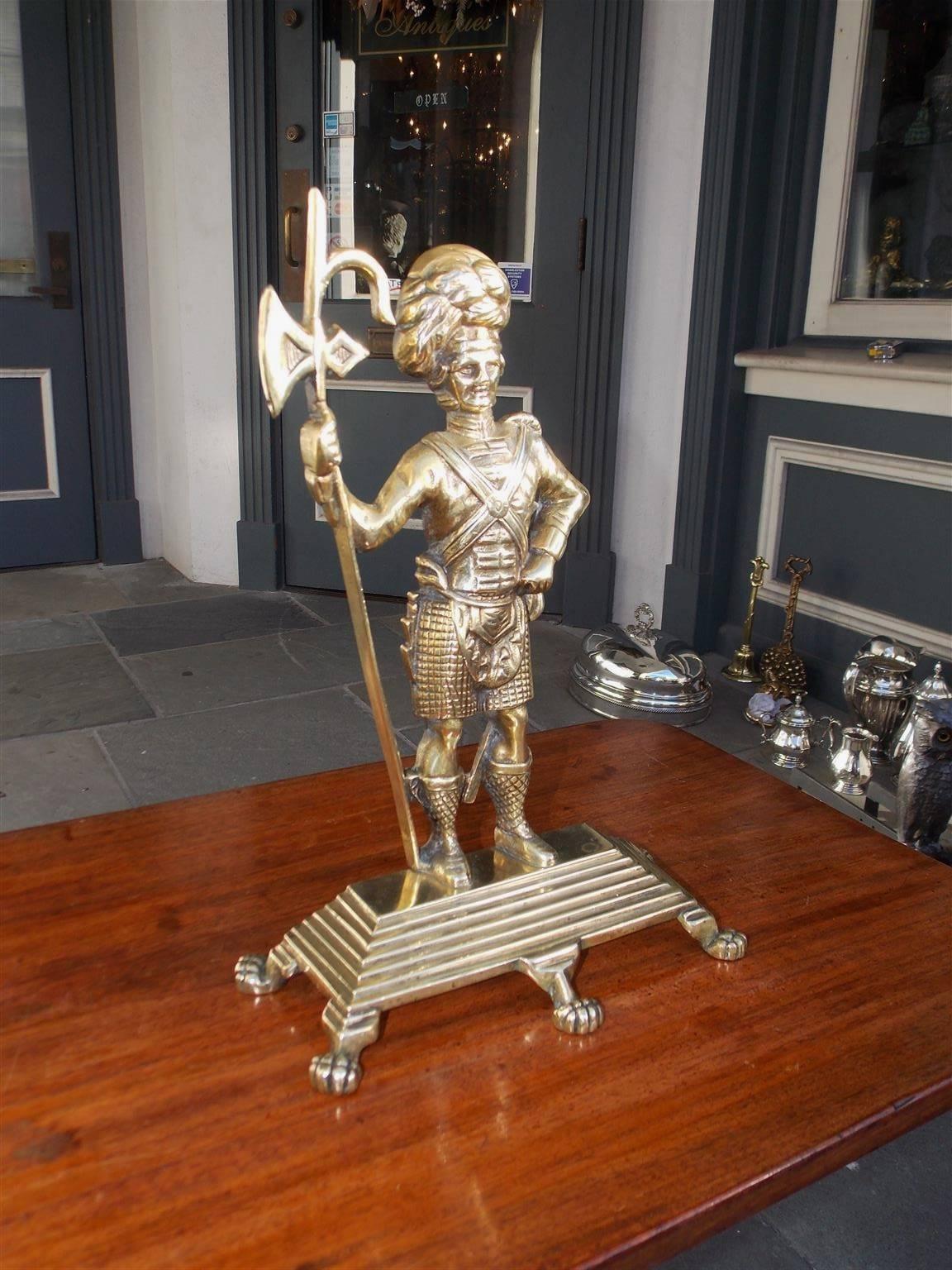 Scottish brass Highlander Royalty Guard doorstop dressed in full military attire standing on a step back rectangular base with lions paw feet, Mid-19th century.