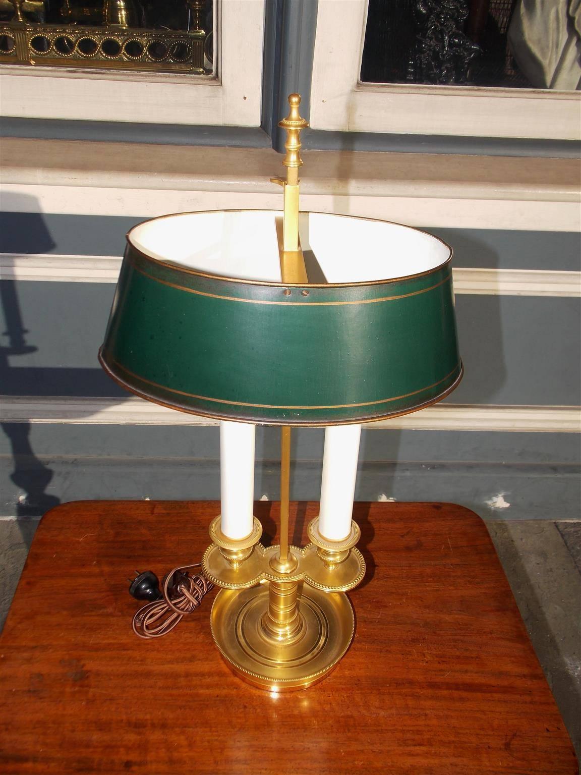 French brass and tole bouillotte table lamp with an centered urn finial , adjustable oval hand-painted and gilt tole shade, two flanking lights, decorative hand chased bead work, and resting on a circular molded base. Early 19th century. Originally
