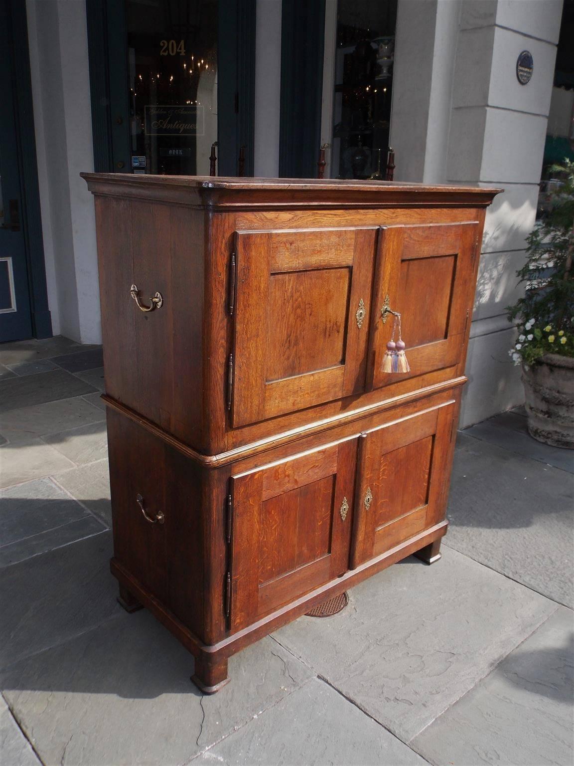 English oak two-piece military Campaign cabinet with a carved molded edge cornice, exposed dovetailing, original brass side handles, hinged upper and lower case doors, fitted interior shelves, original locking mechanisms, and terminating on the