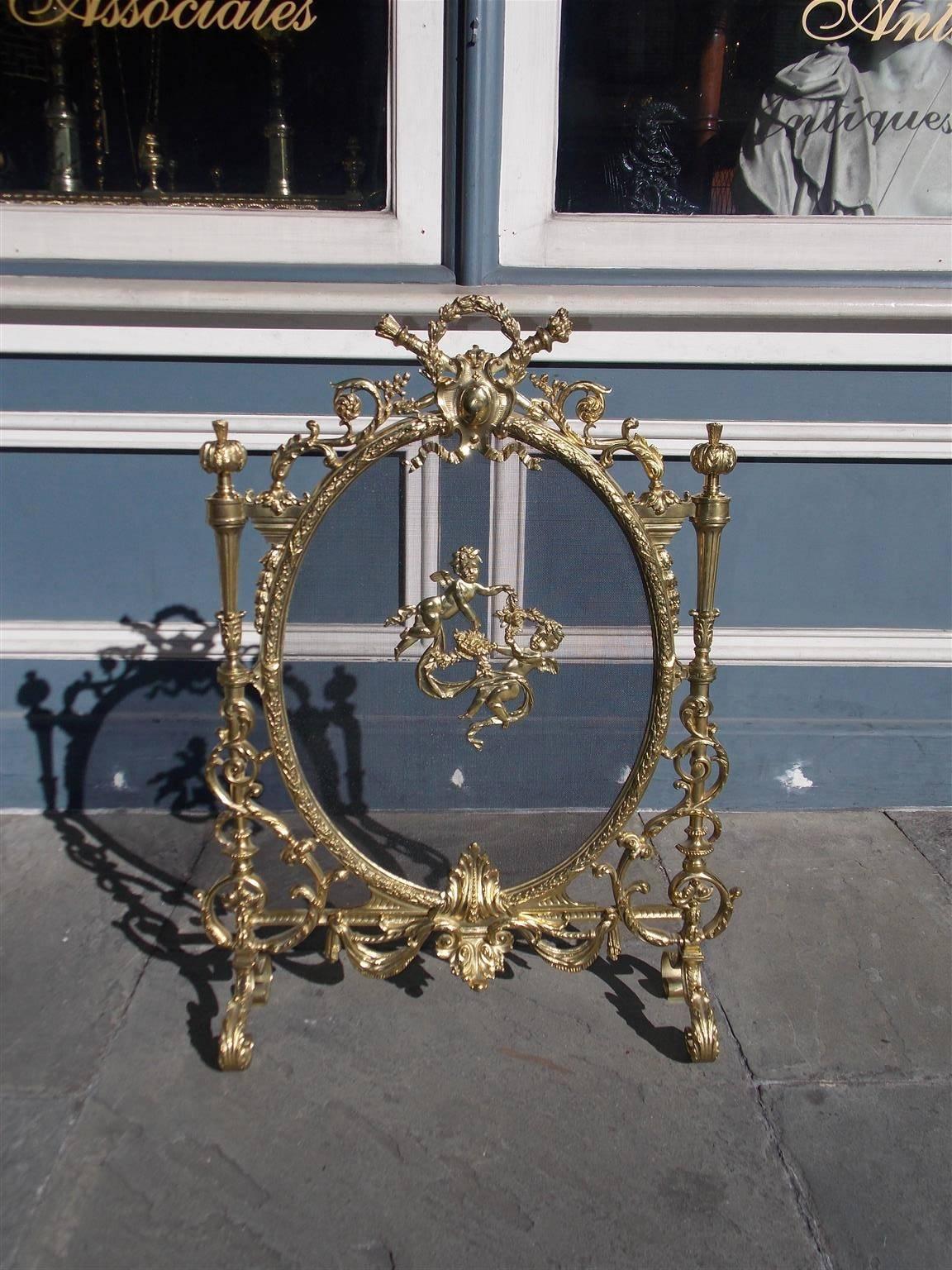 French gilt bronze freestanding fire screen with centered laurel wreath and torch handle, flanking acanthus finials, ribbon and floral scroll work, centered floral cherubs, lower cartouche with swag motif and resting on acanthus scrolled legs, Early