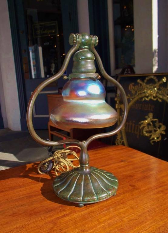 Tiffany Studios bronze desk lamp with original iridescent shade, scrolled bulbous harp, and terminating on circular fluted base with the original circular ball feet. Shade is etched LCT on rim and base is stamped Tiffany Studios 419. New York, Early