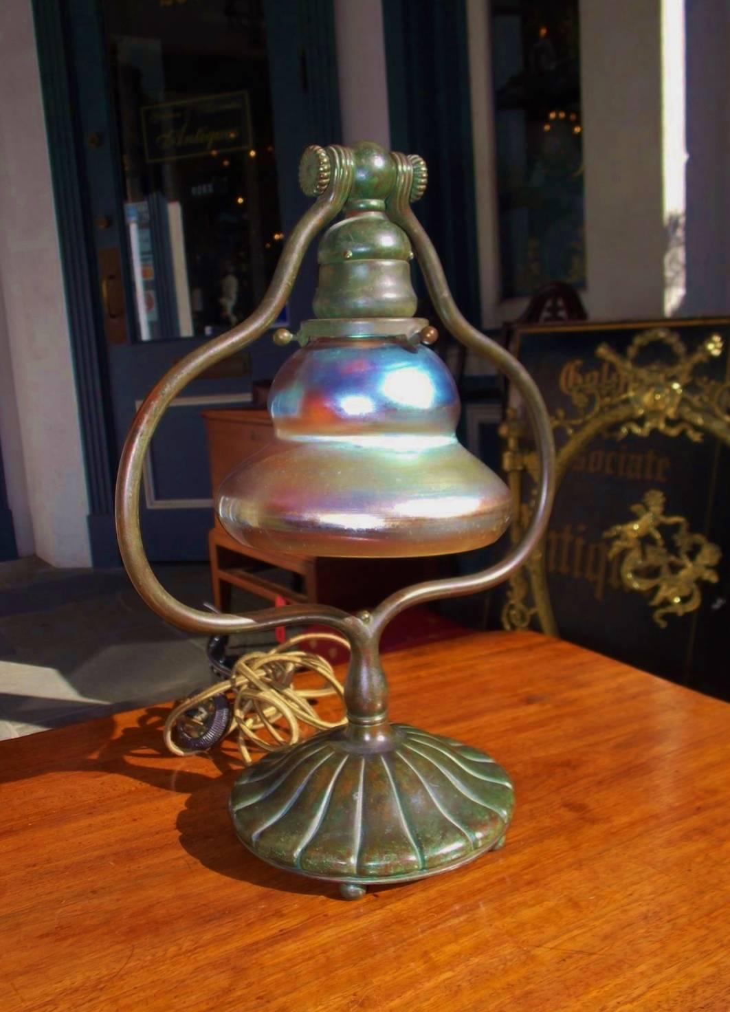 Tiffany Studios bronze desk lamp with original iridescent shade, scrolled bulbous harp, and resting on circular fluted base with the original five ball feet. Shade is etched LCT on rim and base is stamped Tiffany Studios 419, New York. Lamp has the