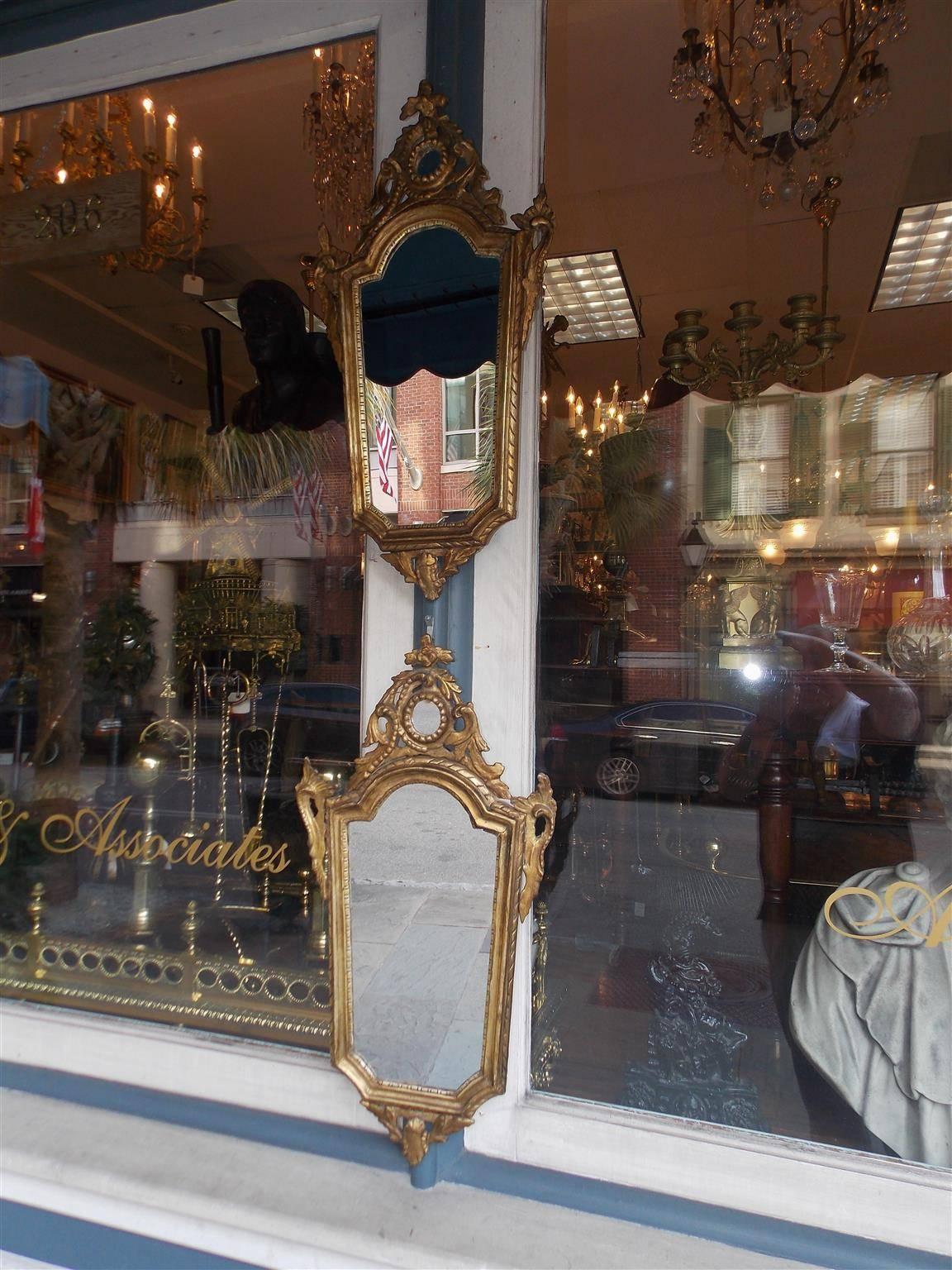 Paire de miroirs muraux italiens en bois sculpté et doré, avec un cartouche floral sculpté, des volutes de feuillage flanquées, un motif intérieur en forme d'œuf et de fléchette, et se terminant par un pendentif floral inférieur. Les miroirs