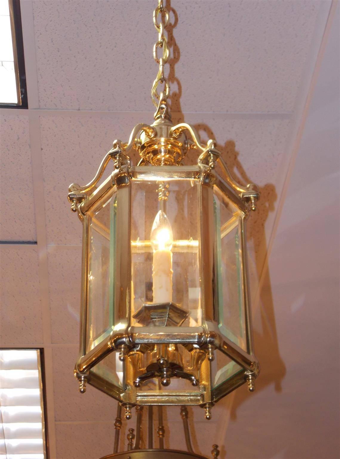 American brass six-sided hall lantern with a centered mounted ring, scrolled arms with corner finials, original beveled glass, three interior light cluster, and resting on a molded edge base with ball finials. Originally candle powered and has been