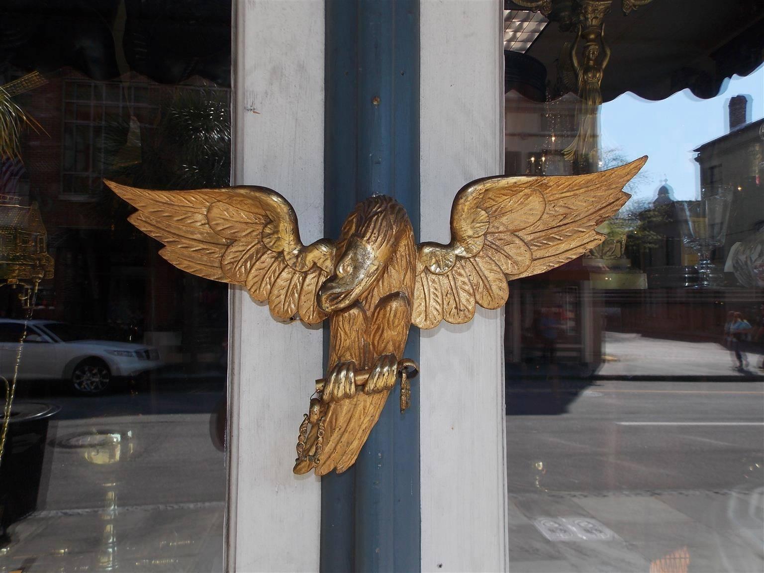 American gilt carved wood and gesso eagle with extended wings grasping gilt rounded bar. Eagle was used for center decoration on drapery rod. Early 19th century.
  
