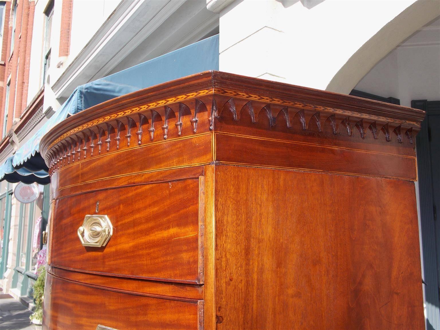 English Hepplewhite mahogany bow front chest on chest with a decorative carved molded edge satinwood inlaid cornice, inverted carved finials ,period brasses, retracting brushing slide, carved lower skirt, and terminating on the original splayed