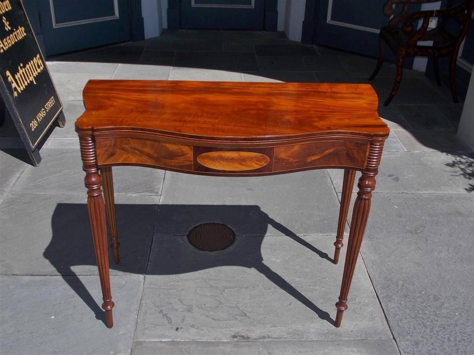 Masterful American Sheraton mahogany hinged top serpentine card table with figured cross banded tulip wood, birch and satinwood inlays, outset corners, and terminating on the original bulbous reeded turned tapered legs, Early 19th Century.