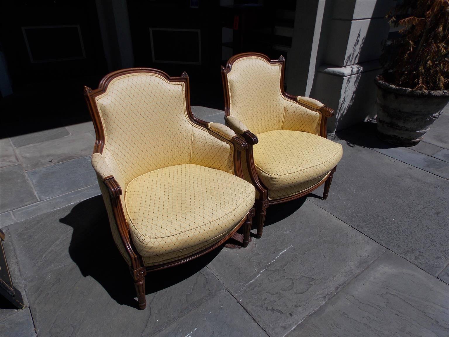 Pair of Italian Walnut Bergere armchairs with carved molded reeded edges, floral corner decorative finials, flanking scrolled arms, floral corner rosettes, and terminating on the original carved fluted ringed legs. Chairs are upholstered in a cross