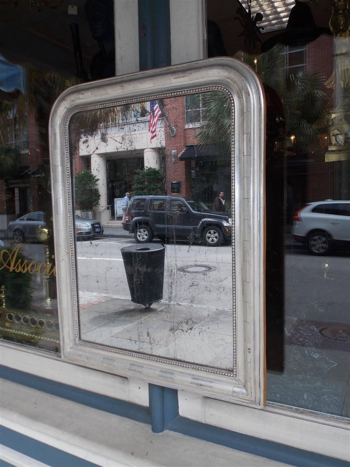 French Louis Philippe silver gilt and gesso mirror with a carved molded edge frame, interior row of beading, original silvered glass, and retains the original wood backing, Early 19th Century.