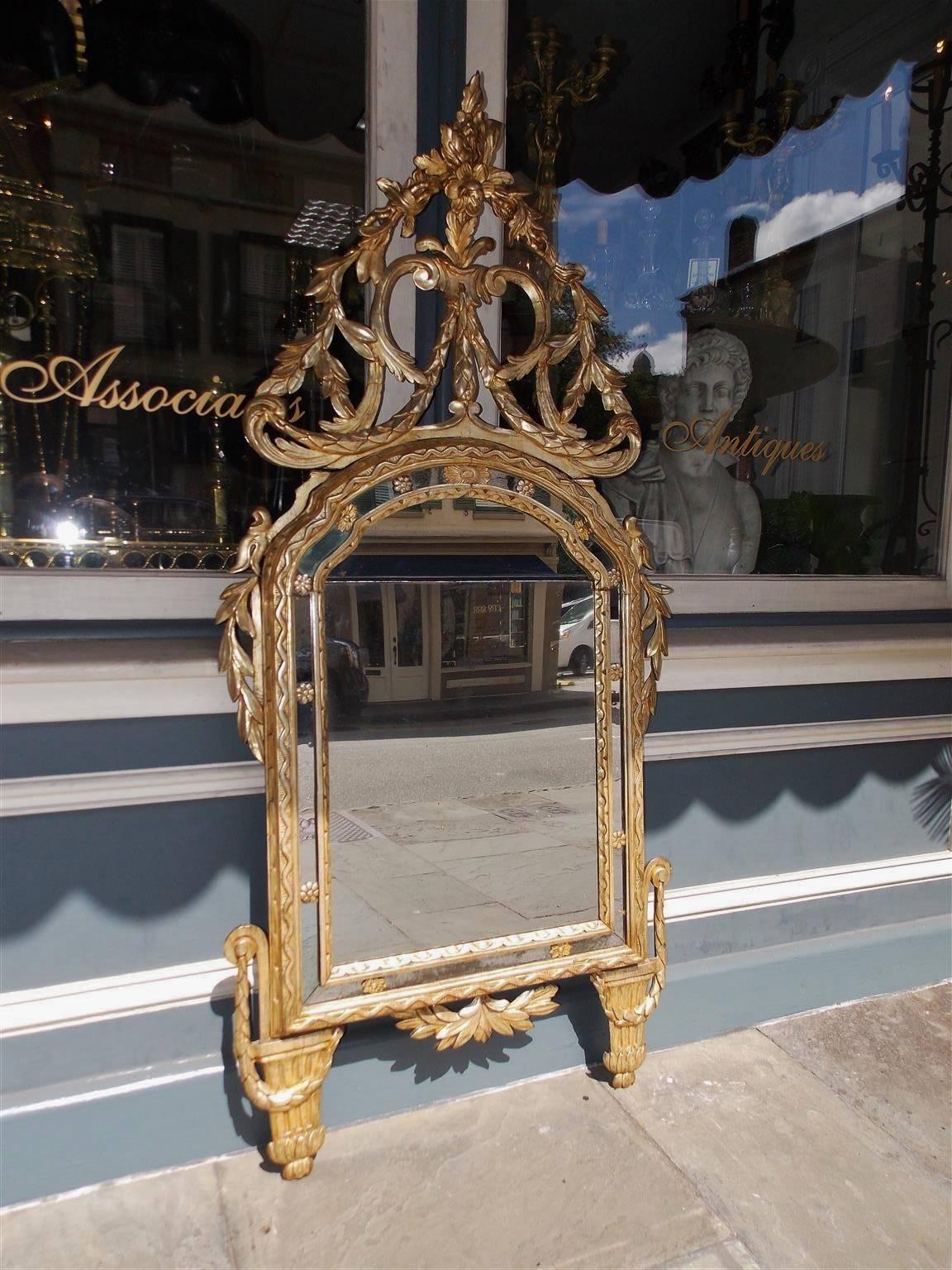 Italian neoclassical silver and gold gilt carved wood & gesso wall mirror with a foliage scroll work cartouche, arched mirror plate with molded rosette surrounds, flanked by foliage garlands, and terminating on decorative fluted molded feet.