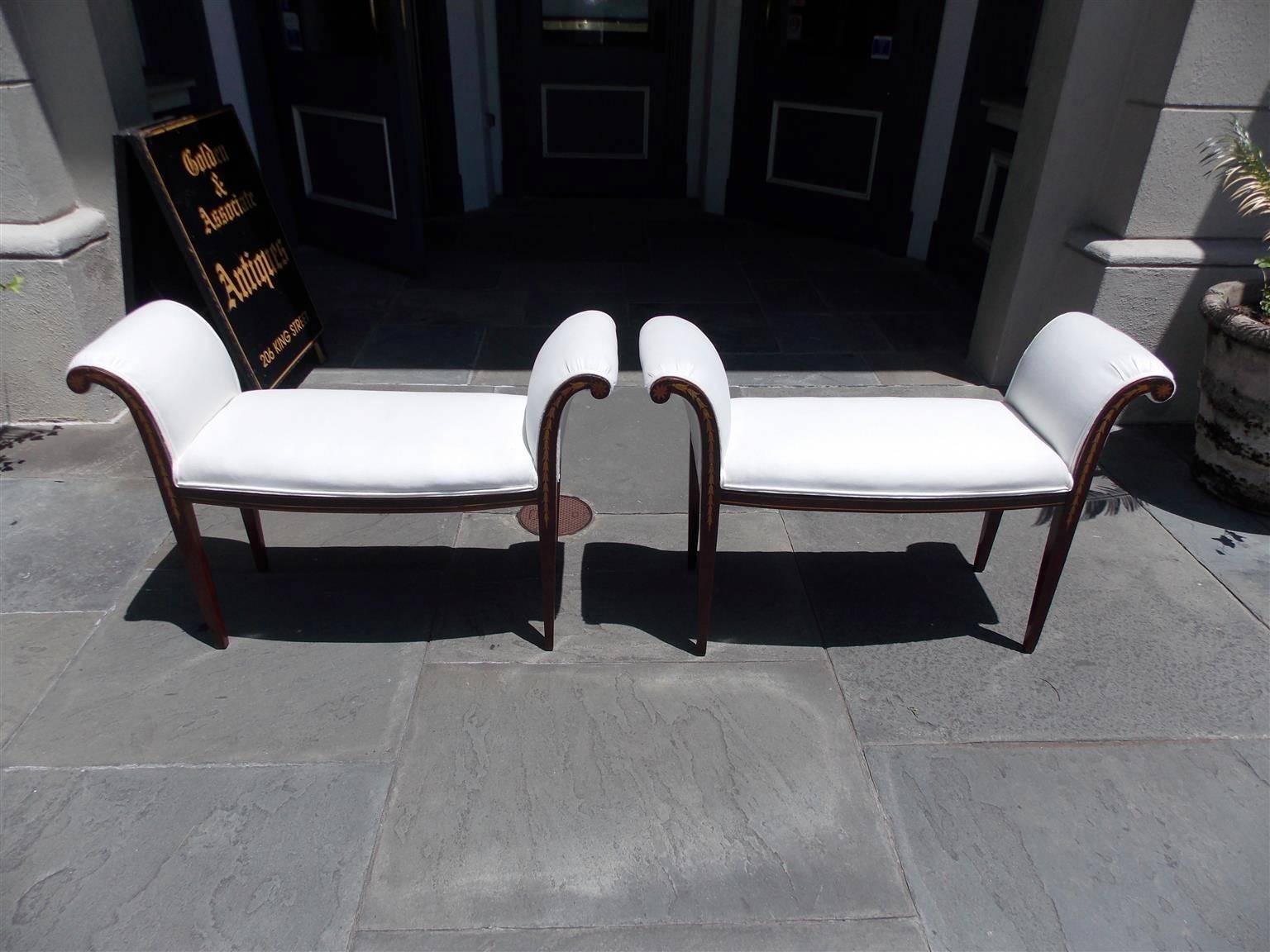 Pair of English mahogany window benches with flanking scrolled arms, floral medallions, graduated satinwood inlaid bell flowers, and terminating on tapered squared legs. Benches are upholstered in white muslin, Early 19th century.