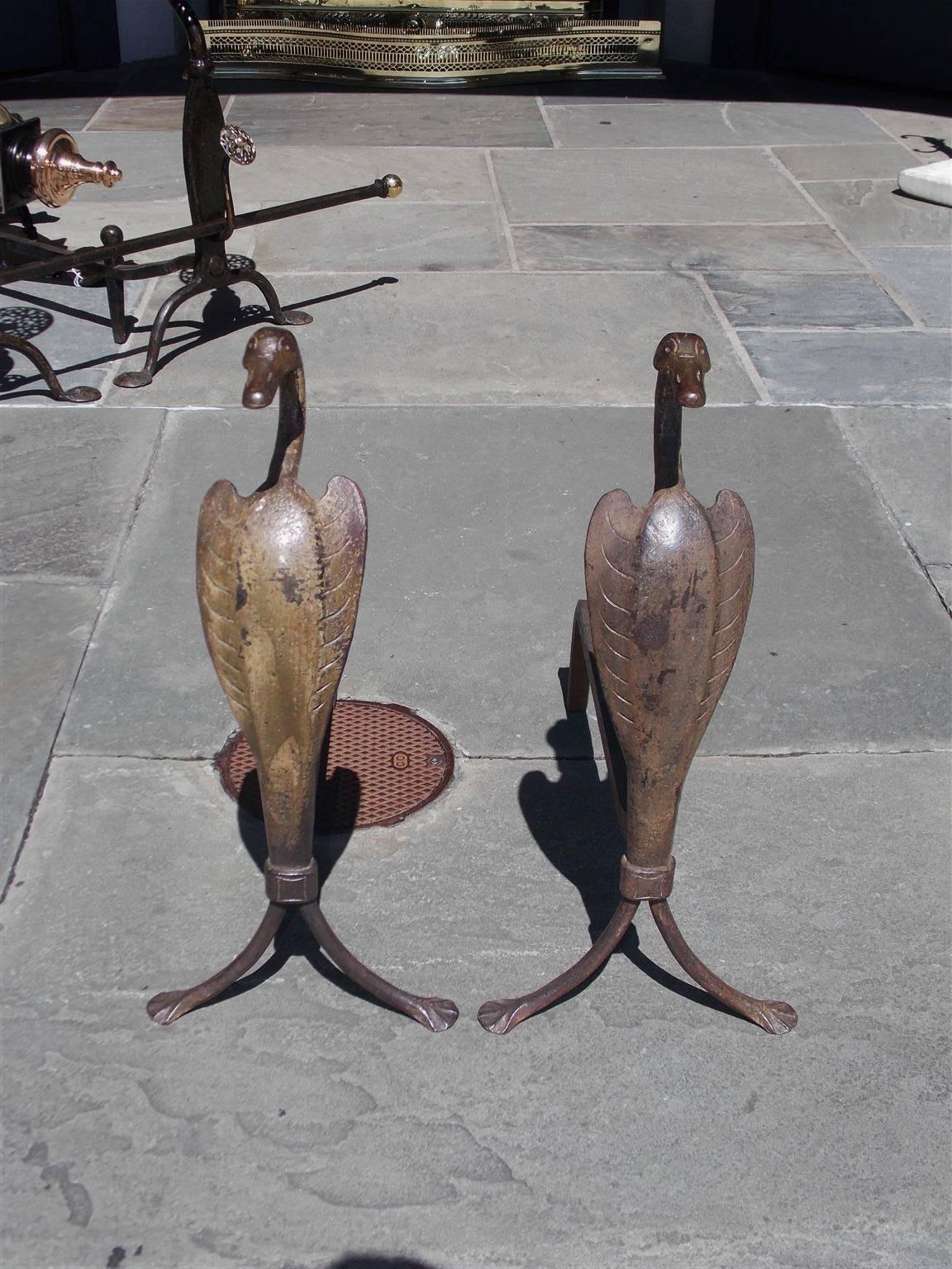 Pair of American cast iron egret andirons with flanking scrolled decorative heads, hand chased side feathers, original iron dog legs, and terminating on splayed stylized web feet, Early 20th century.