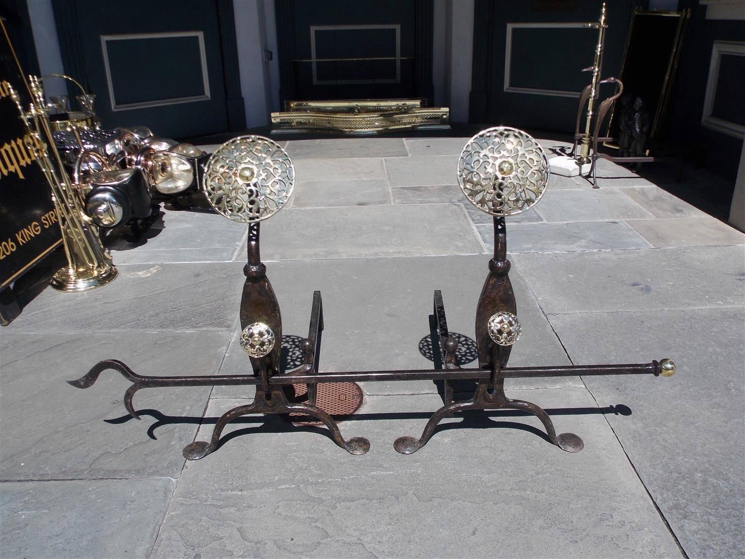 Pair of English brass and cast iron decorative floral double medallion andirons with molded plinths, spit hooks with poker, matching ball log stops, and terminating on scrolled legs with penny feet, Mid-19th century. Cast iron and brass ball top