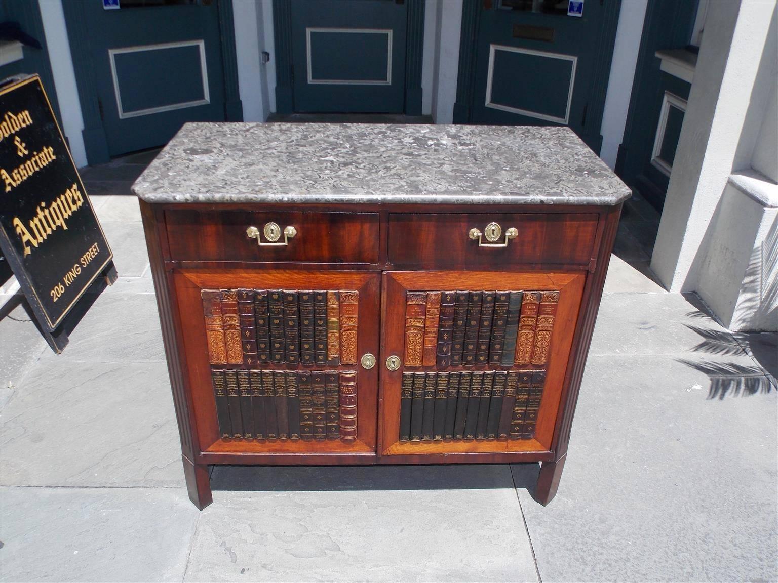 English Regency mahogany two-drawer cabinet with the original grey and white breccia marble-top, original brasses, fluted side columns, flanking faux leather hinged bookcase doors revealing interior shelving, and resting on the original block feet,