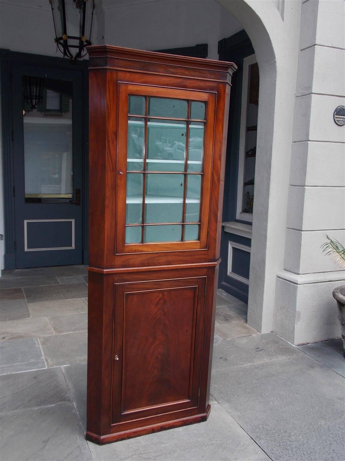 American Federal two-piece mahogany and rosewood diminutive corner cabinet with a carved molded edge cornice, upper hinged mullion glass door with three fitted interior shelves, lower hinged blind door with two fitted interior shelves, resting on
