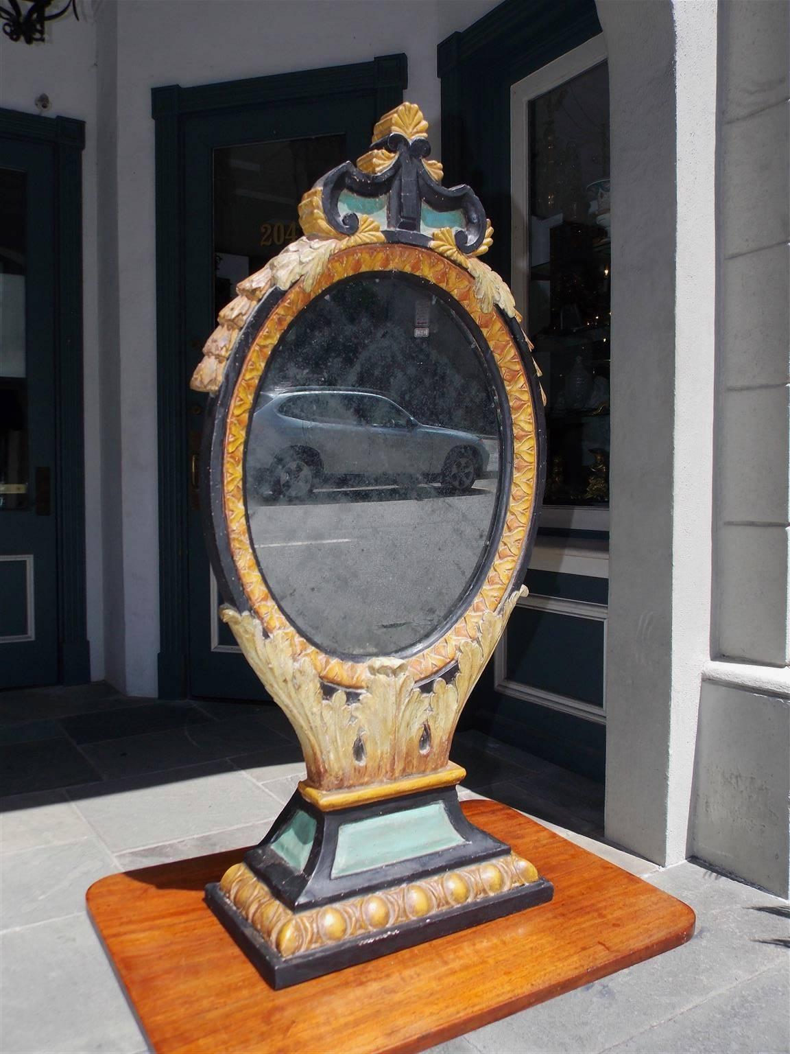 Italian gilt and painted oval dressing - shaving mirror with decorative scrolled floral cartouche, flanking bell flowers, interior decorative lambs tongue frame resting on acanthus carved step back egg and dart plinth. Piece retains the original