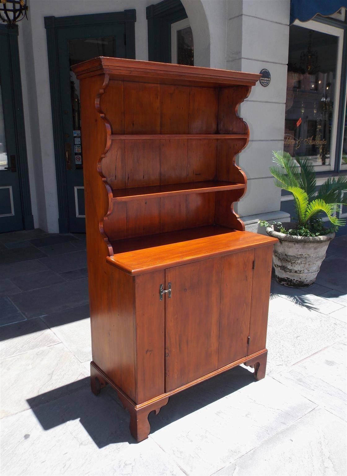 American white pine step back cupboard with a carved molded edge cornice, upper case flanking carved scalloping with two exterior shelves, single hinged locking lower case door with interior fitted shelf, and resting on the original carved bracket