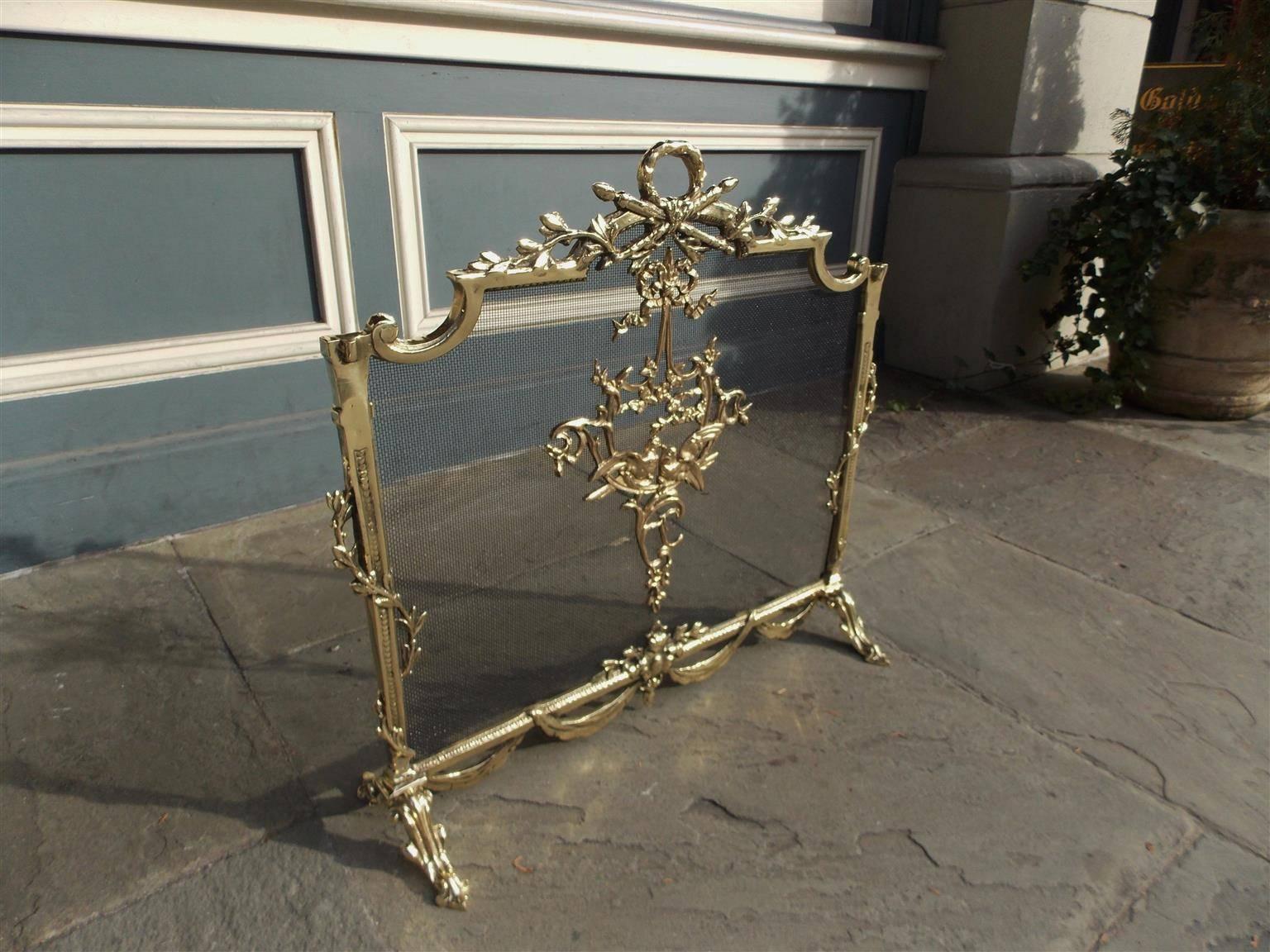 French brass freestanding fire place screen with a foliage Laurel wreath handle crossed by torchieres, centered ribbon, doves, and floral medallion, flanking floral intertwined beaded borders, lower ornament with connecting swags, and terminating on