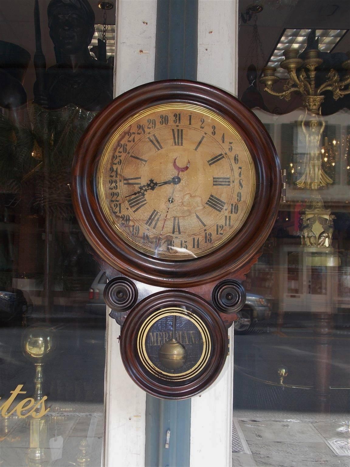 American faux painted rosewood calendar clock with circular molded edge surround, hinged glass upper door reveling the original paper face with Roman and Arabic  numerals, flanking carved ringed medallions, and a lower hinged reverse glass painted