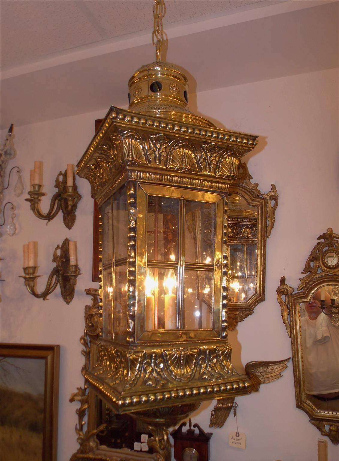 French brass square hanging hall lantern with vented circular dome, upper molded and beaded edge shell border, paneled hinged glass doors, lower molded and beaded edge shell border, and terminating on circular inverted chased floral dome with