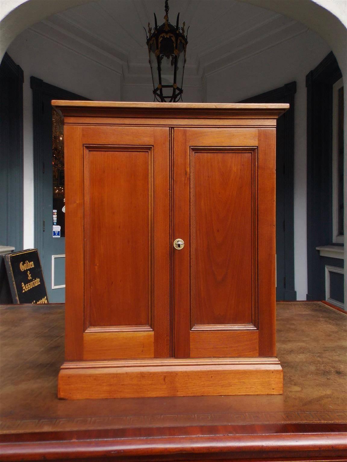 American walnut blind door display cabinet with fitted interior lined drawers, ebonized knobs, original lock with key, and resting on a carved molded edge base. 
Late 19th century.