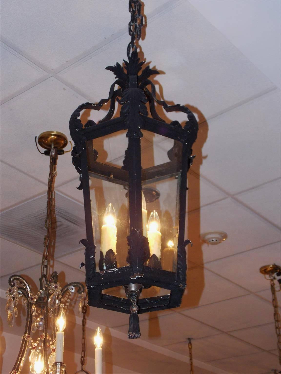 French Hexagon cast iron and painted hall lantern with upper scrolled acanthus arms, interior three light cluster surrounded by six glass panels, lower acanthus decoration, and terminating with a centered hanging decorative painted and gilt tassel.