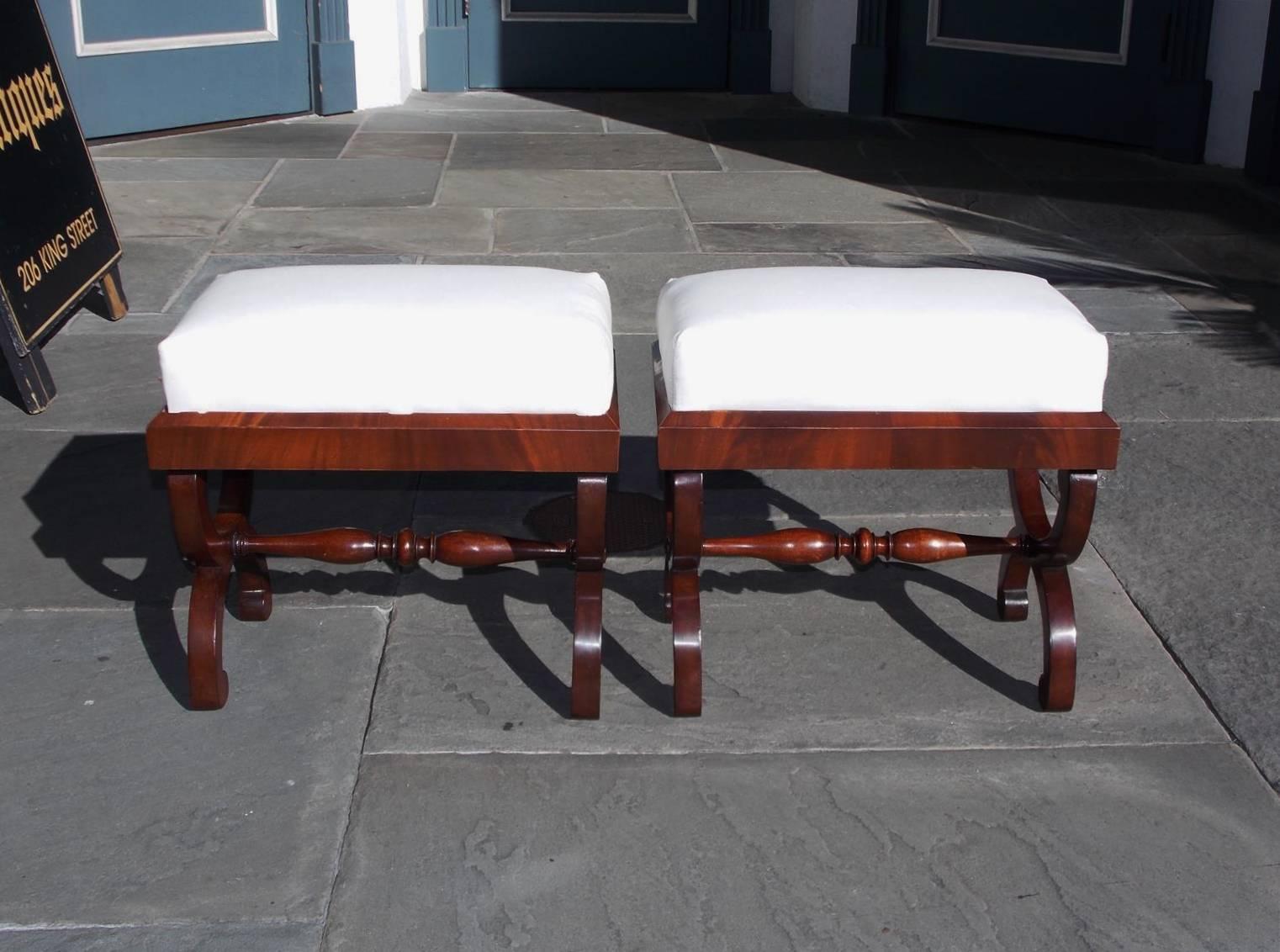 Pair of American Classical mahogany Curule stools with carved molded edges, turned bulbous stretchers and resting on scrolled flanking scrolled legs, Early 19th century. Stools are upholstered in white muslin.