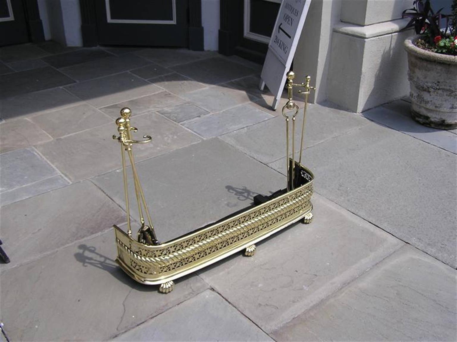 English brass rope and ivy motif fireplace fender with the original three-piece tool set and tool holders. Early 19th Century. Set consist of shovel, tong, and poker.