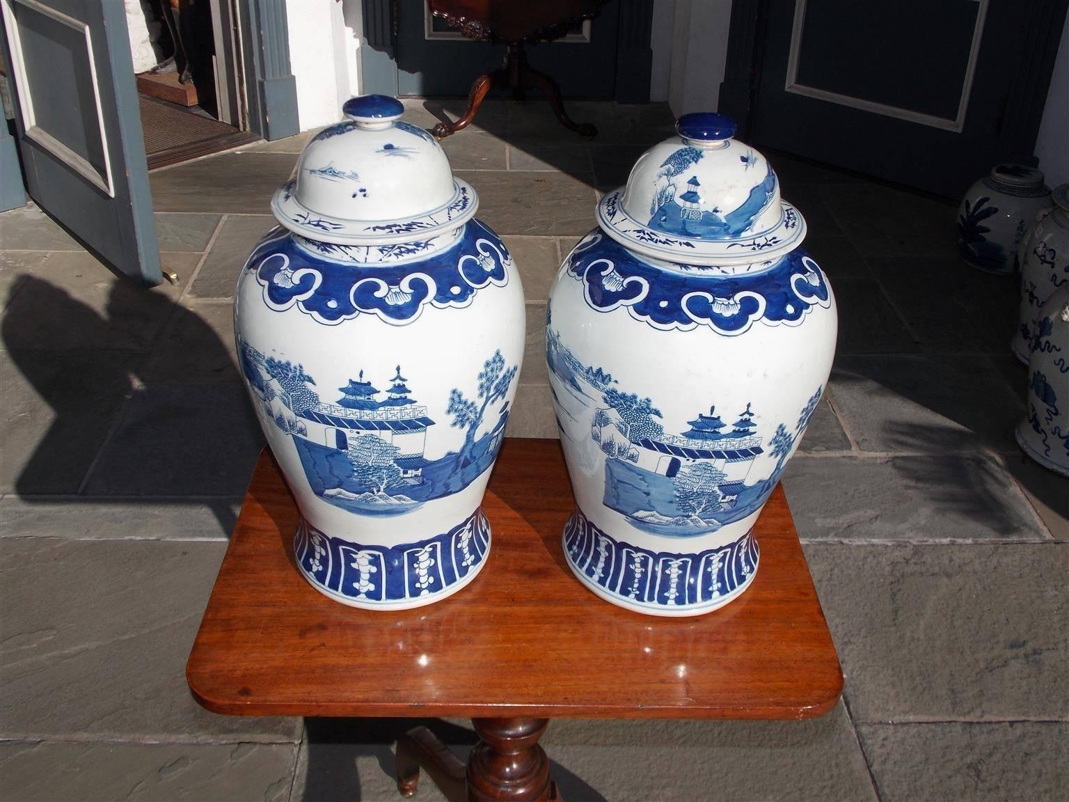 Pair of Chinese porcelain glazed blue and white temple jars with hand-painted decorative borders, trees, pagodas, landscapes, and running stream scenes. Lids are removable and were used to store perishable goods, 20th century.