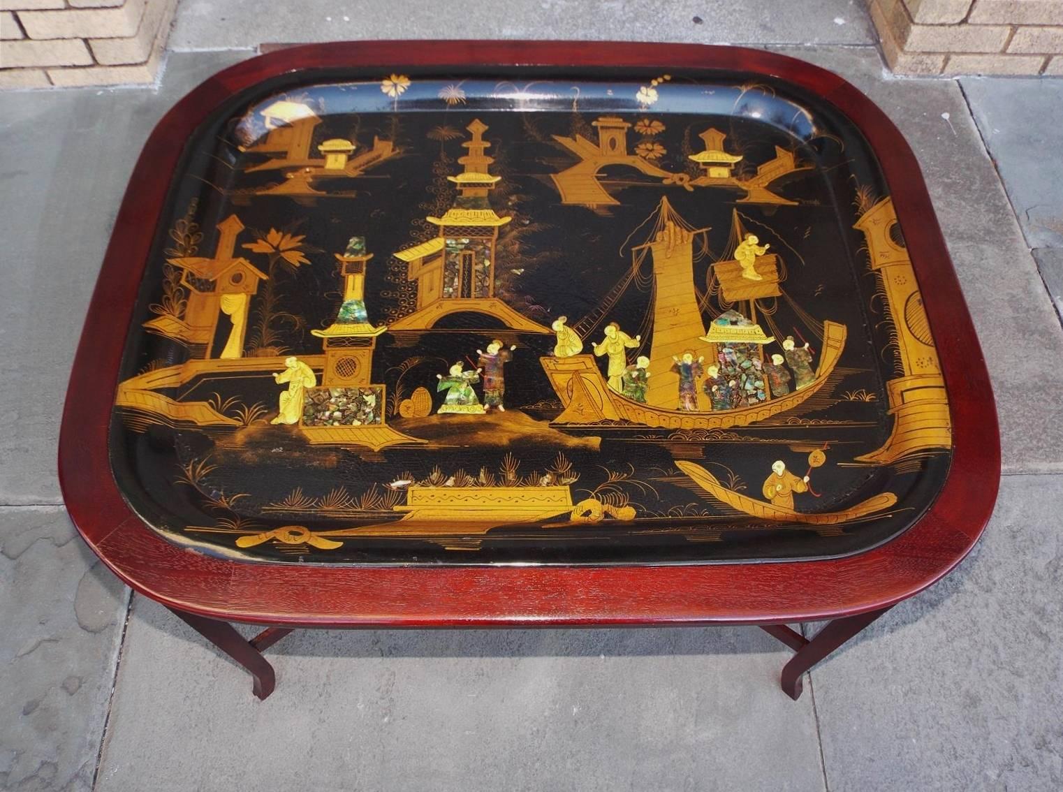 English Chinoiserie gilt paper mâché tray on stand with decorative abalone carvings, sailing ships, pagodas, landscape scenes, and resting on a mahogany stand with splayed feet and connecting stretchers, Early 19th century.