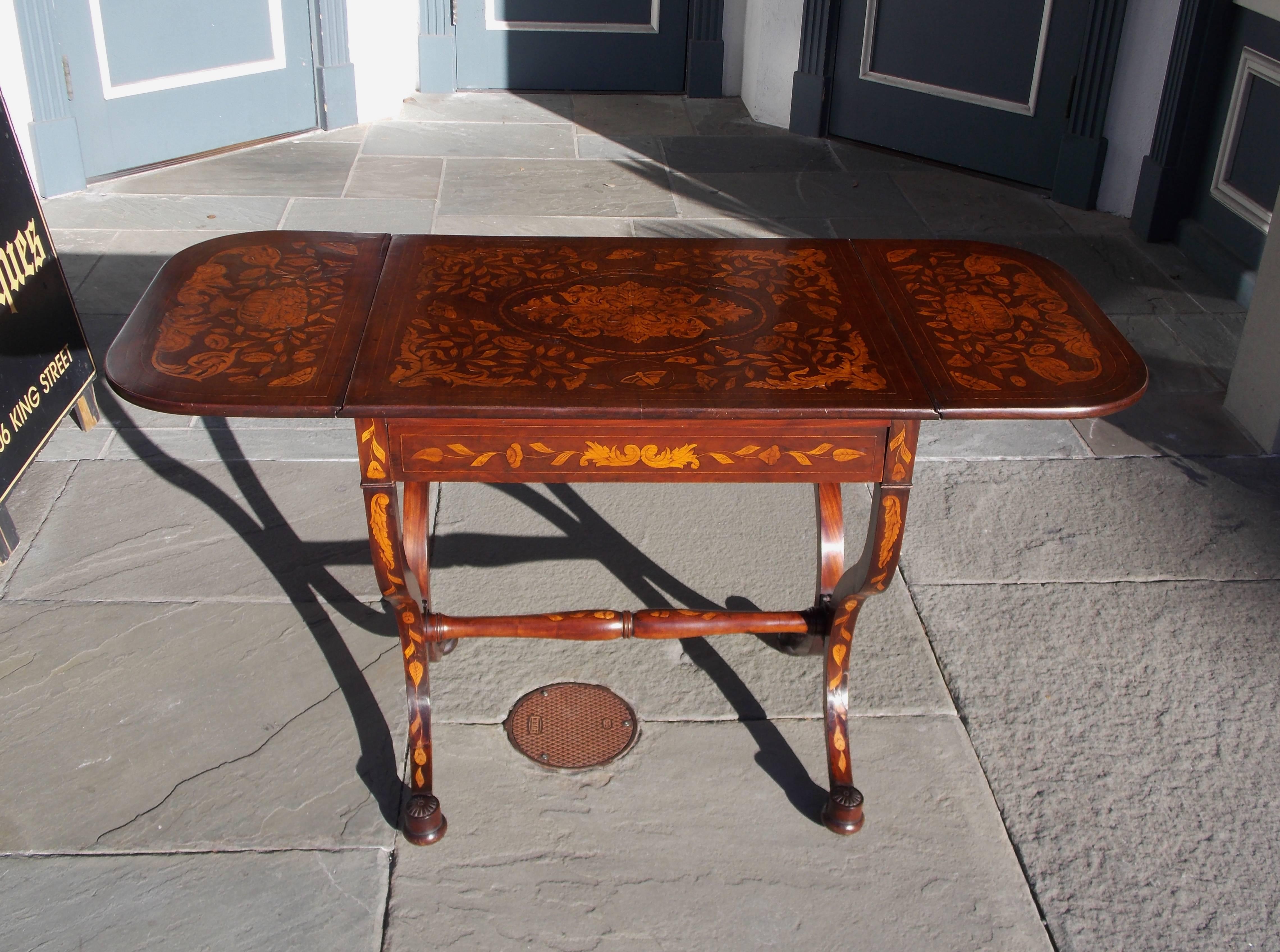 Dutch Regency Kingwood one drawer drop leaf marquetry library table with satinwood inlaid foliage and butterflies, centered decorative inlaid floral medallion, two drop leaves with flanking floral urn baskets, carved rosettes , and terminating on