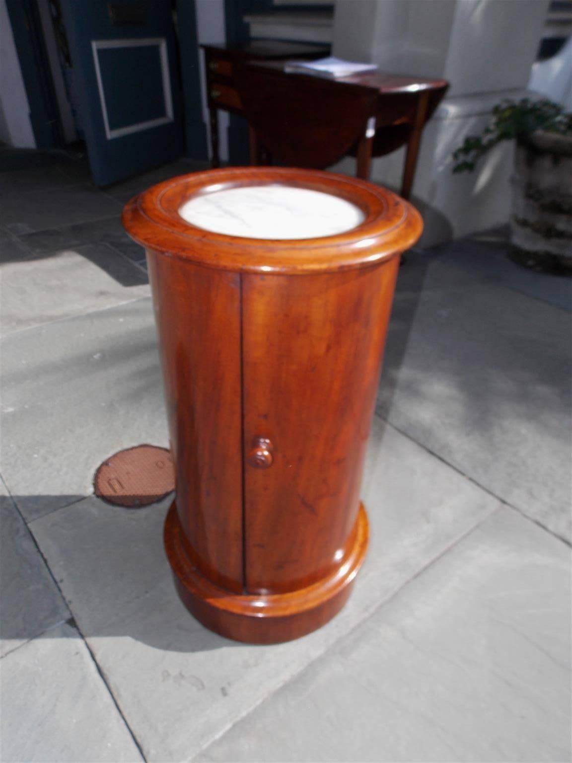 English Regency mahogany and marble-top pedestal commode with a carved molded edge top, original wood knob, hinged door with interior shelf , and terminating on a circular carved molded edge base, Early 19th century.